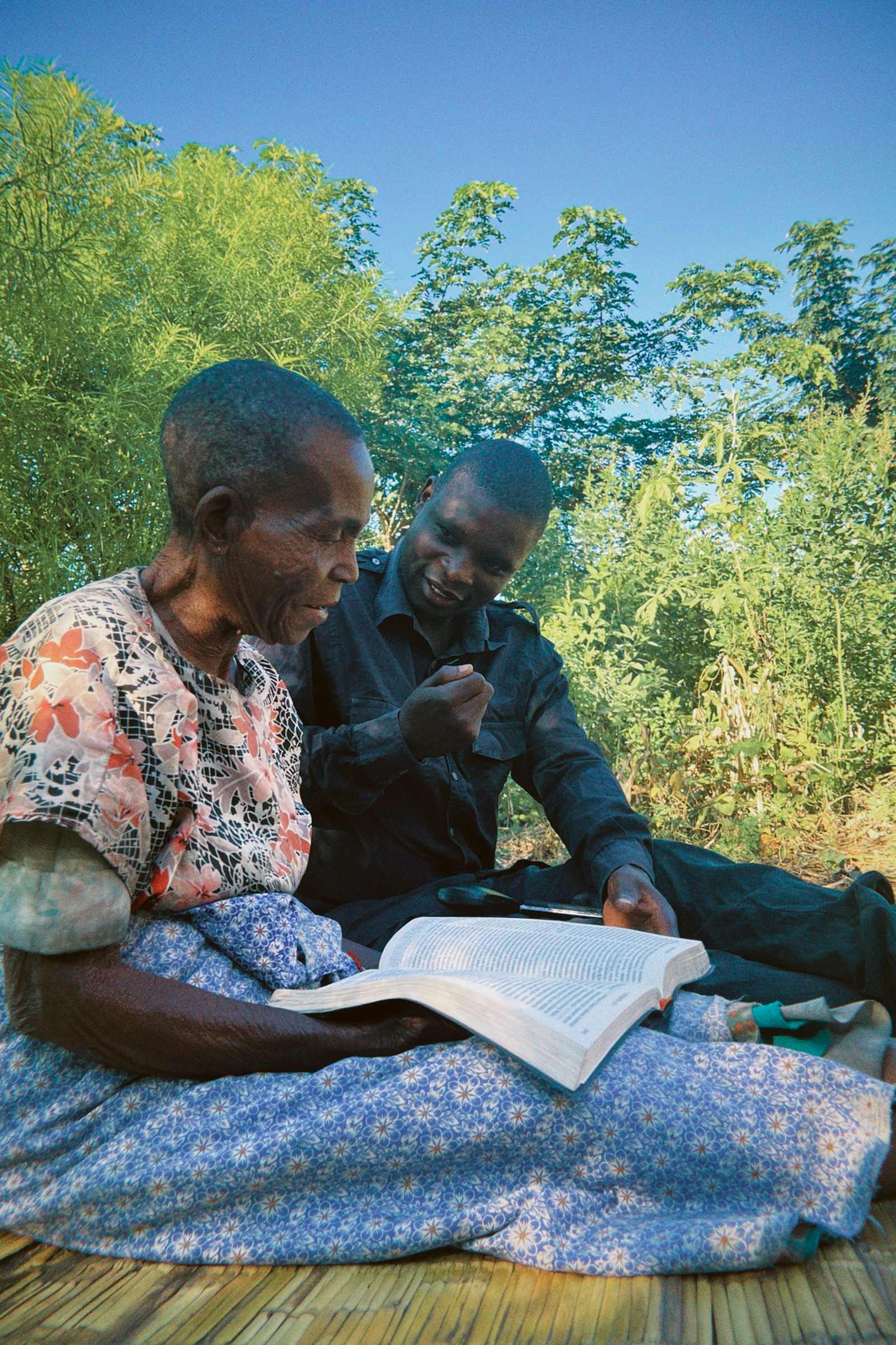 Agogo aakazi ndi mwamuna akuwerenga Baibulo pamodzi, atakhala pa mphasa panja